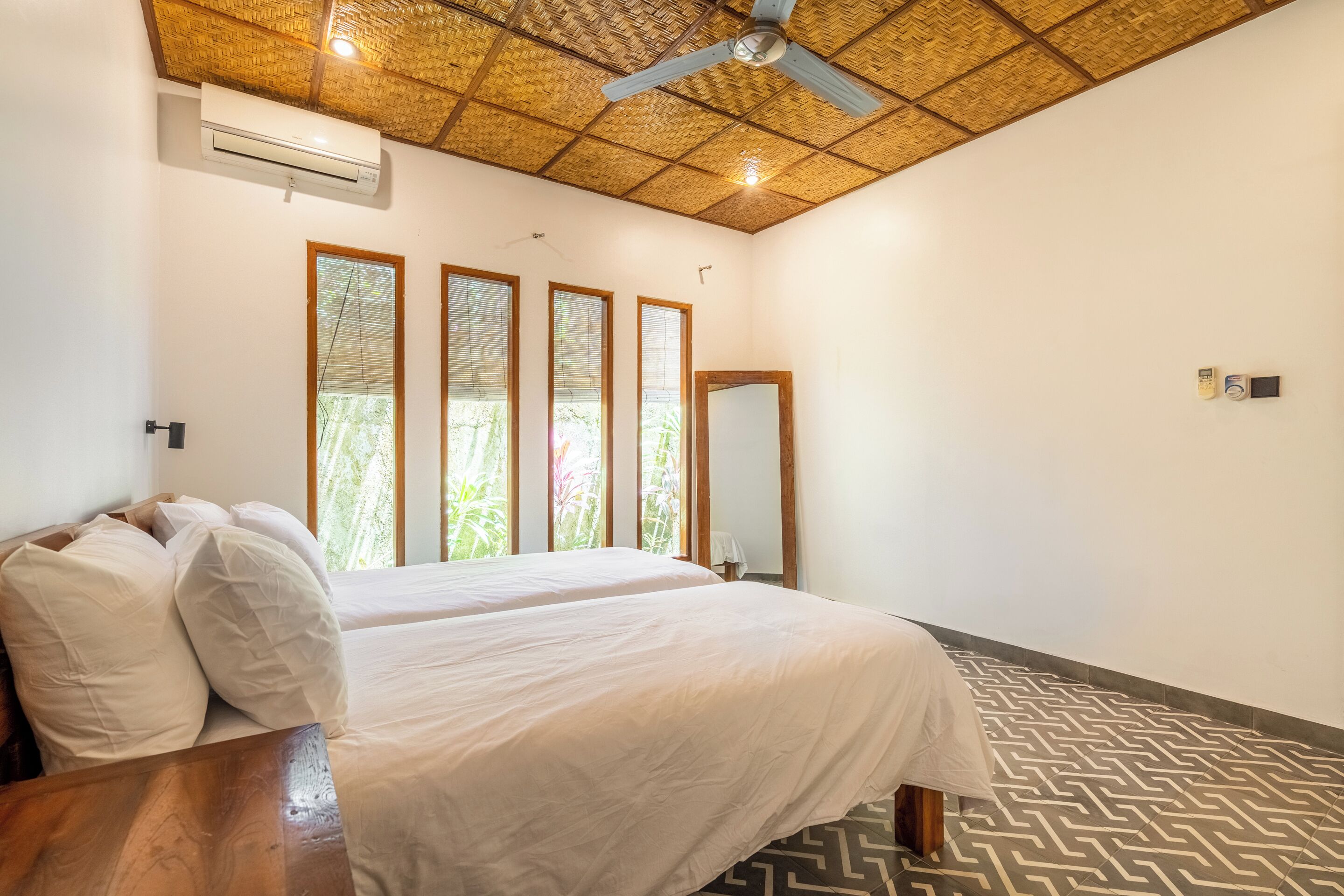 A bedroom with two beds, a ceiling fan, and a large window with blinds.
