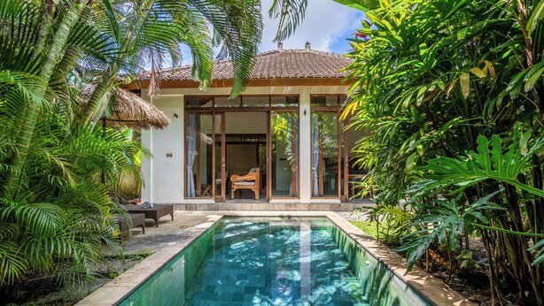 Un espace aménagé au bord de la piscine, avec une maison, une chaise et une végétation luxuriante.