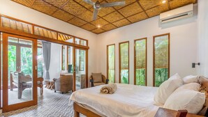 Une chambre à coucher avec un grand lit, une tête de lit en bois et une vue sur l’extérieur grâce à de grandes fenêtres.