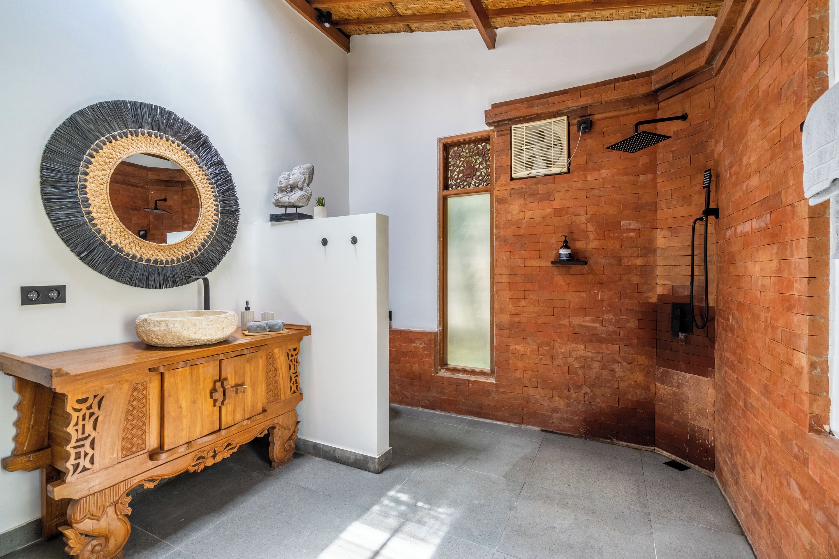 Un baño con tocador de madera, un espejo redondo, ducha con pared de ladrillo y un armario blanco.