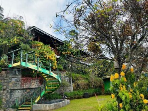 A traditional house with a stone wall and a green staircase leading to a wooden deck. - THE KODAI HAVEN (Kodaikanal)