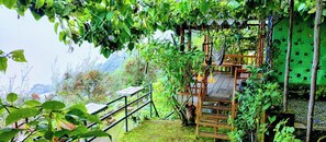 A wooden deck with a hammock, surrounded by lush greenery and a view of mountains.