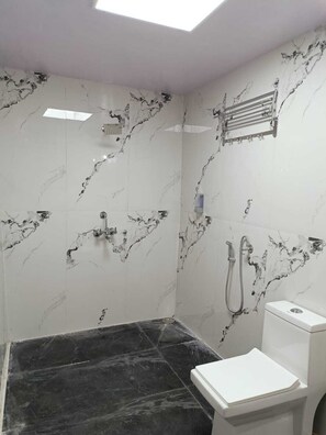 A bathroom with white marble walls and a black marble floor, a toilet, and a shower area. - THE KODAI HAVEN (Kodaikanal)