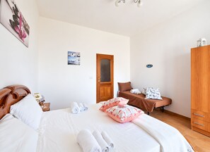 A bedroom with a bed, a wooden wardrobe, a door, and a wall with a picture.