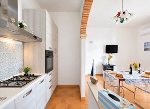 A modern kitchen with a gas stove, oven, and a dining area with a table set for two. - Seaside Villa Golden Shell 1 (Porto Cesareo)