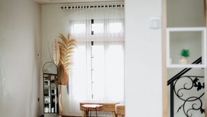 A room with a wooden floor, a round table, a wicker chair, a mirror, and a large plant. - Roadsidevilla's (Kejajar)