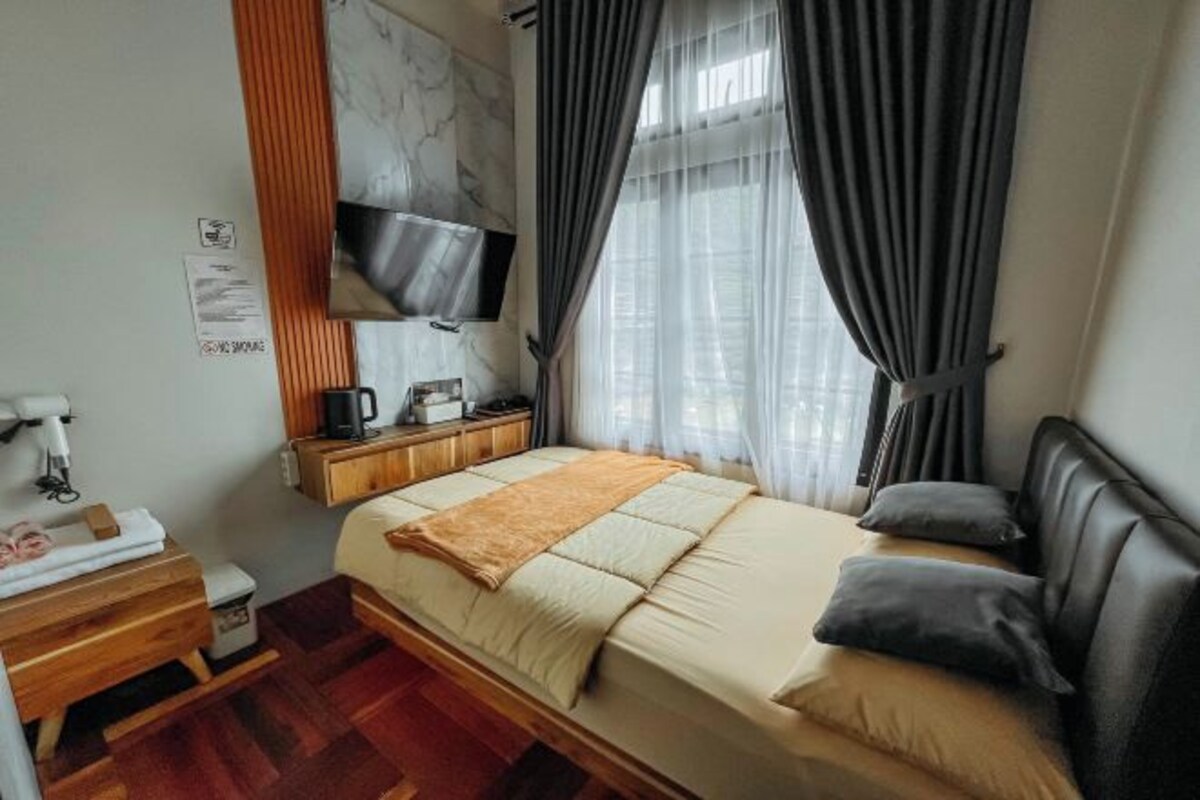 A modern hotel room with a large bed, a wooden nightstand, a flat-screen TV, and a window with curtains.