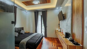 A modern hotel room with a bed, wooden floor, a TV mounted on the wall, and a window with curtains. - Roadsidevilla's (Kejajar)