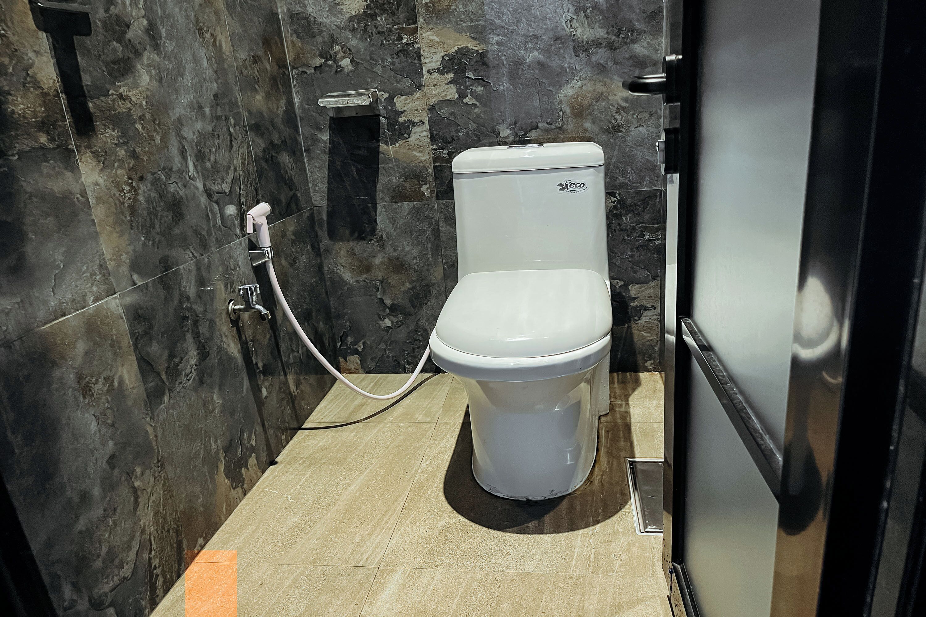 A compact bathroom with a white toilet, a marble wall, and a tiled floor.