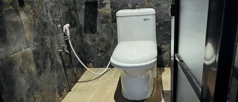 A compact bathroom with a white toilet, a marble wall, and a tiled floor.