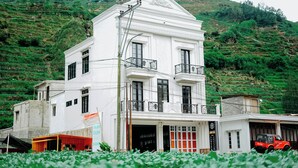 A white two-story building with balconies, a garage, and a signboard. - Roadsidevilla's (Kejajar)
