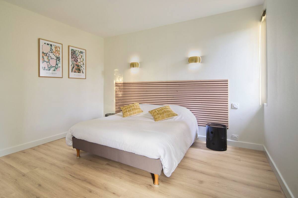 A bedroom with a bed, wooden floor, two wall-mounted lights, and two framed pictures.