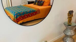 A bedroom with a bed, a round mirror, a small statue, and a basket. - The colors of Commarin 2-bedroom apartment with kitchen. (Commarin)