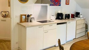 A compact kitchen with white cabinetry, a stainless steel range hood, and a dining area with a wooden table and chairs. - The colors of Commarin 2-bedroom apartment with kitchen. (Commarin)