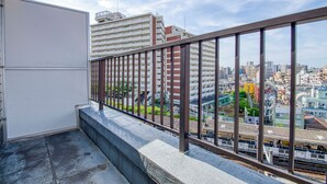 A balcony with a metal railing overlooking a cityscape with buildings and a train track. - CraftFlat Komagome 604 (豊島区)