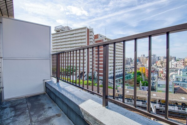 A balcony with a metal railing overlooking a cityscape with buildings and a train track.