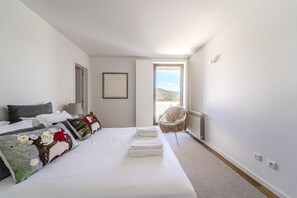 Ein Schlafzimmer mit einem großen Bett, einem Sessel und Blick ins Freie.