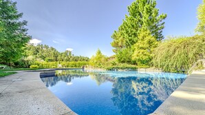 A swimming pool with a clear blue water surface, surrounded by lush greenery and trees. - Ge House by House and People (Caniçada)
