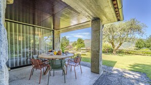 An outdoor patio with a round table and chairs, large windows, and a view of a grassy landscape. - Ge House by House and People (Caniçada)