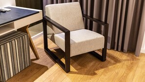Ein Stuhl mit Holzgestell und gepolstertem Sitz, auf einem Holzboden, mit einem gestreiften Ottoman neben ihm.