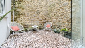 Ein Innenhof mit Steinwänden, zwei weißen Korbstühle, davon einer mit rotem Kissen, und ein kleiner runder Tisch mit einem pinken Kissen.