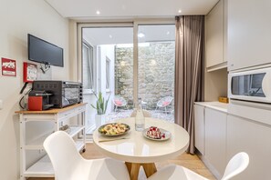 A compact kitchen with a dining table, chairs, a TV, and a stone wall view.