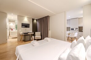 Una habitación de hotel moderna con una cama grande, un escritorio, una silla, un televisor y una kitchenette.