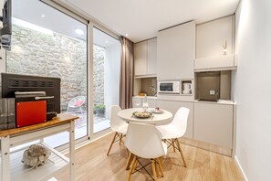 Una cocina moderna con comedor, que incluye una mesa redonda con sillas blancas, horno empotrado y una pared de piedra visible a través de la puerta de cristal.