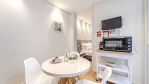 Eine kompakte Küche mit Mikrowelle, kleinem Kühlschrank und Essbereich mit weißen Stühlen und einem runden Tisch.