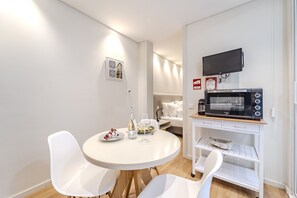 A compact kitchen with a microwave, a small refrigerator, and a dining area with white chairs and a round table.