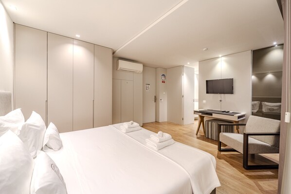 A modern hotel room with a large bed, a desk, a chair, and a TV.