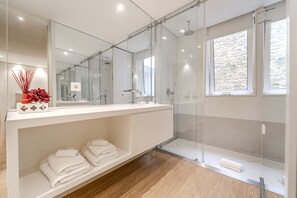 Un baño moderno con cabina de ducha de vidrio, un espejo grande y suelo de madera.