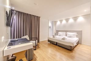 Ein modernes Hotelzimmer mit Holzboden, einem Bett mit weißer Bettwäsche, einem Schreibtisch mit Computer und einem an der Wand befestigten Fernseher.