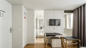 A modern hotel room with a wooden floor, a desk with a chair, a TV mounted on the wall, and a window with curtains. - Sé inn 4 by House and People (Braga)