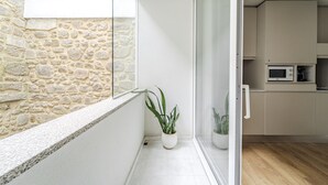 A modern kitchen with a stone wall, a potted plant, and a sliding glass door leading to a balcony. - Sé inn 4 by House and People (Braga)