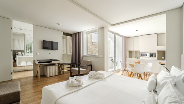 A modern hotel room with a large bed, a desk, a TV, and a kitchenette. - Sé inn 4 by House and People (Braga)