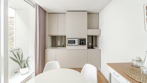 A modern kitchen with white cabinets, a microwave, and a dining area with a white table and chairs. - Sé inn 4 by House and People (Braga)