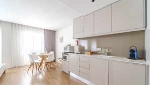 Una cocina moderna con armarios blancos, un microondas y un lavamanos. Hay una zona de comedor con una mesa redonda y sillas.