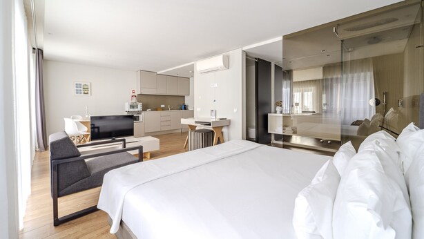 Una habitación de hotel moderna con una cama grande, un escritorio, una silla y una kitchenette.