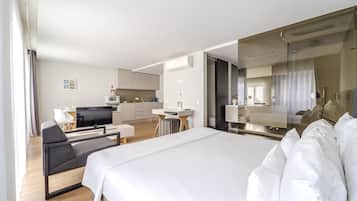 A modern hotel room with a large bed, a desk, a chair, and a kitchenette.