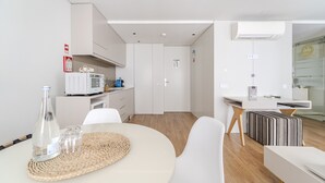 Una cocina moderna con armarios blancos, microondas y cafetera. Cuenta con un comedor con una mesa redonda y sillas, y una pequeña zona de kitchenette con refrigerador y microondas.