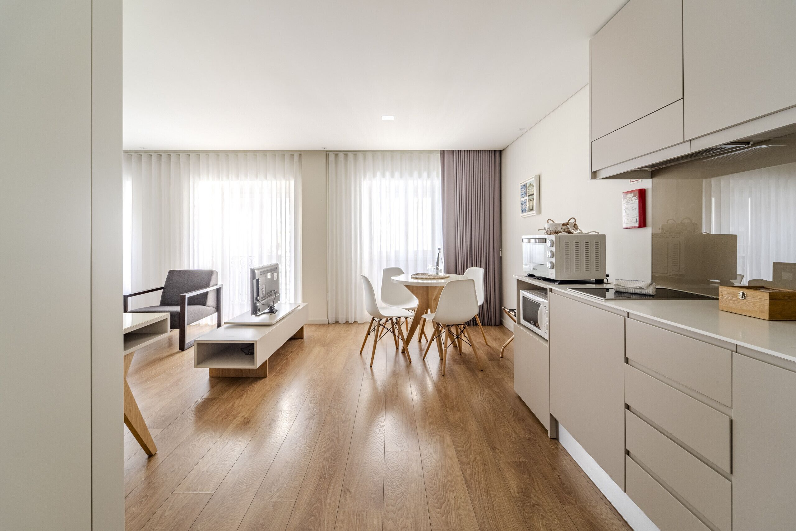 A modern kitchen with wooden flooring, a dining area with white chairs, and a built-in oven.