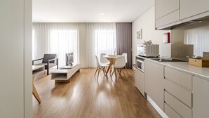 Una cocina moderna con suelo de madera, una zona de comedor con sillas blancas y un horno empotrado.