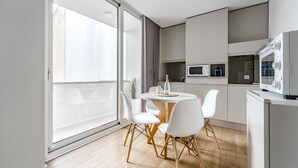 Ett modernt kök med matplats, med ett runt bord och vita stolar, samt en stor skjutdörr i glas som leder ut till en balkong.