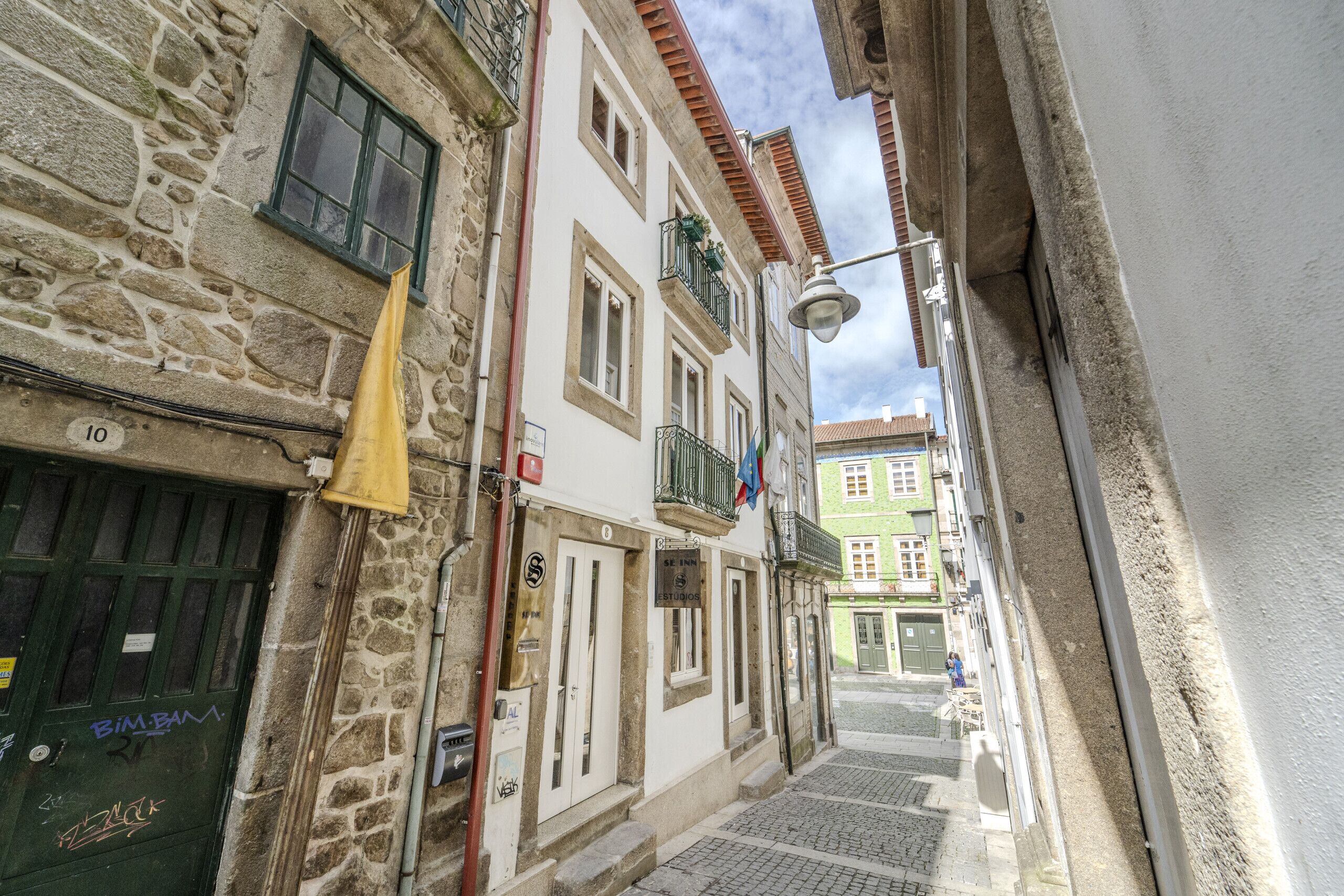 A narrow street with stone buildings, a green flag, and a sign for 'Estudio 10'.
