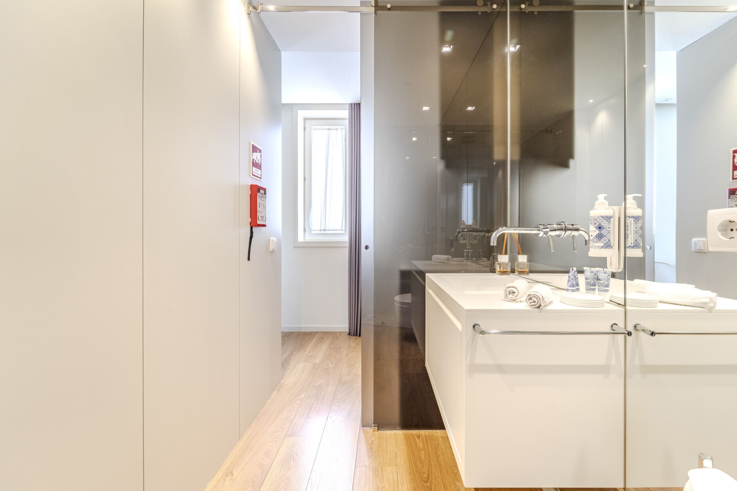 A modern bathroom with a glass shower enclosure, a white sink with toiletries, and a wooden floor.
