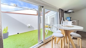 A modern room with a sliding glass door leading to a small garden, a round table with chairs, and a kitchenette area.