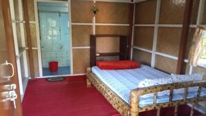 A single bed with a wooden frame and a red mattress, a small red bucket, and a window with a view of a blue door. - N Palky Camp By GRB (Chariduar Circle)