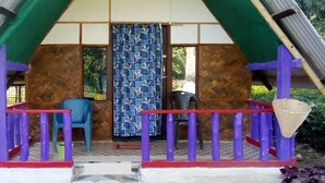 A small, single-room structure with a sloped roof, a balcony with a red railing, and a woven basket hanging on the right side. - N Palky Camp By GRB (Chariduar Circle)