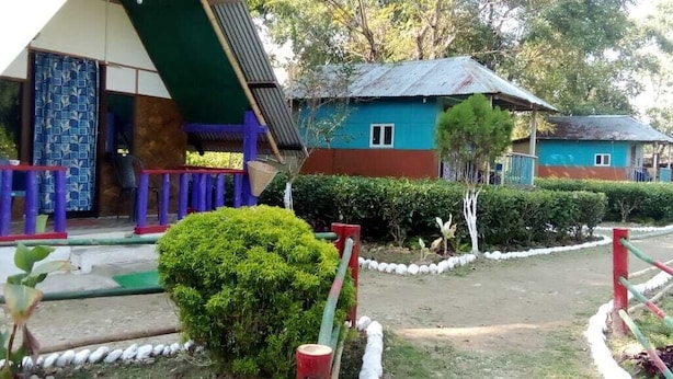 A colorful building with a sloped roof, surrounded by well-maintained gardens and a fenced pathway. - N Palky Camp By GRB (Chariduar Circle)